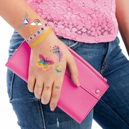 Hand with colorful temporary tattoos holding a pink wallet.