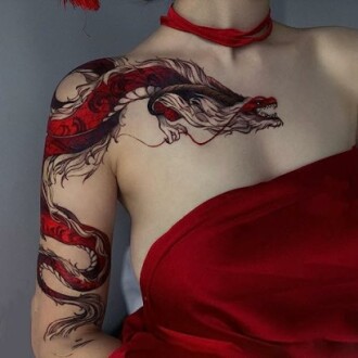 Person with a detailed dragon tattoo on shoulder and arm, wearing a red garment.