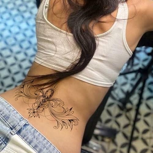 Woman with floral lower back tattoo wearing white top and jeans.